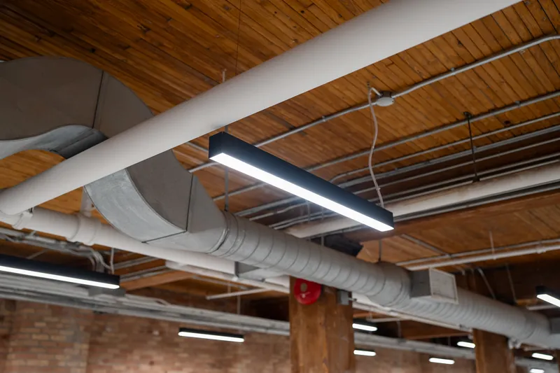 Linear LED fixtures hung beneath exposed ductwork in a brick-and-timber loft