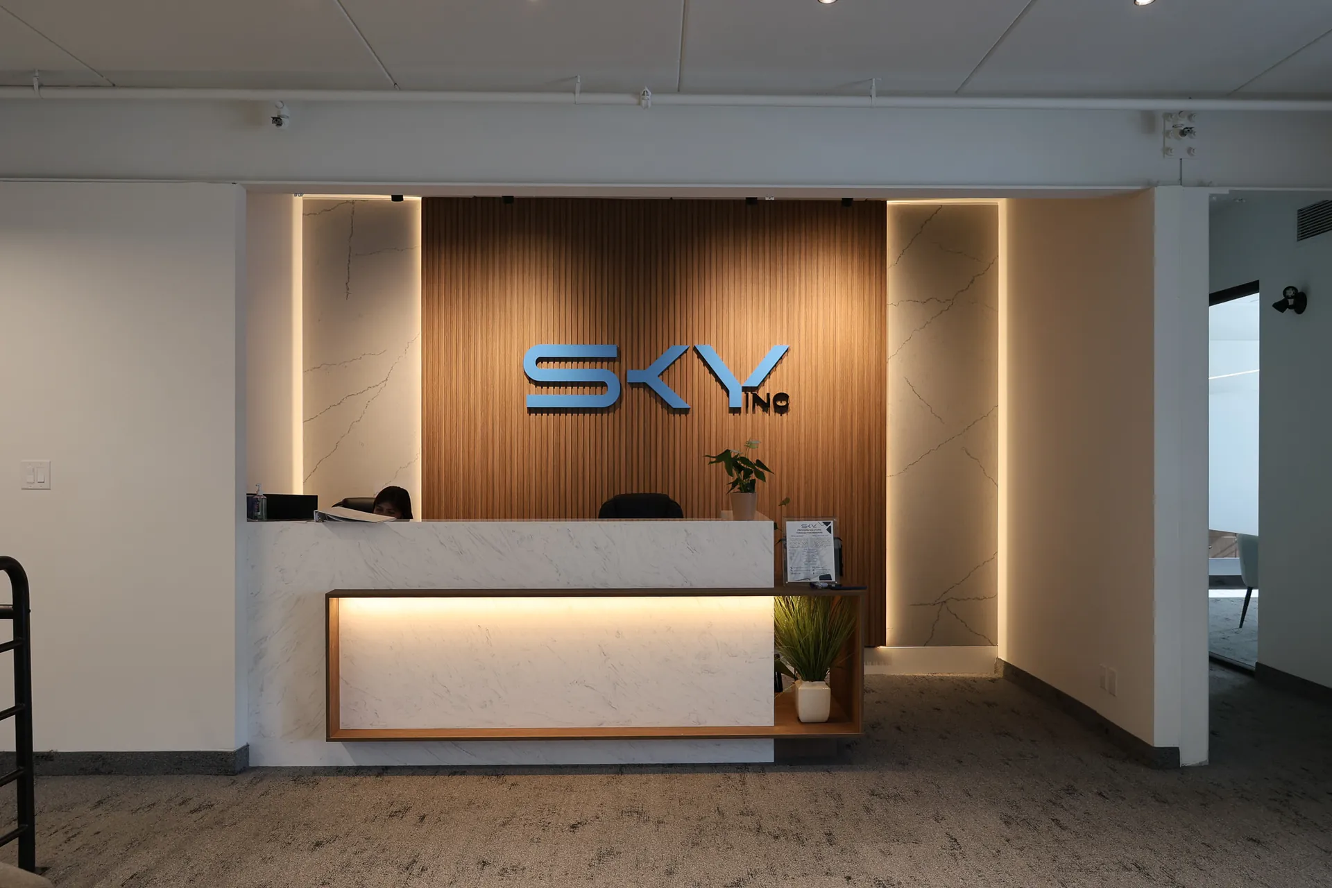 Sky Contracting reception — the SKY Inc logo on a backlit wood-slat feature wall behind a white marble desk