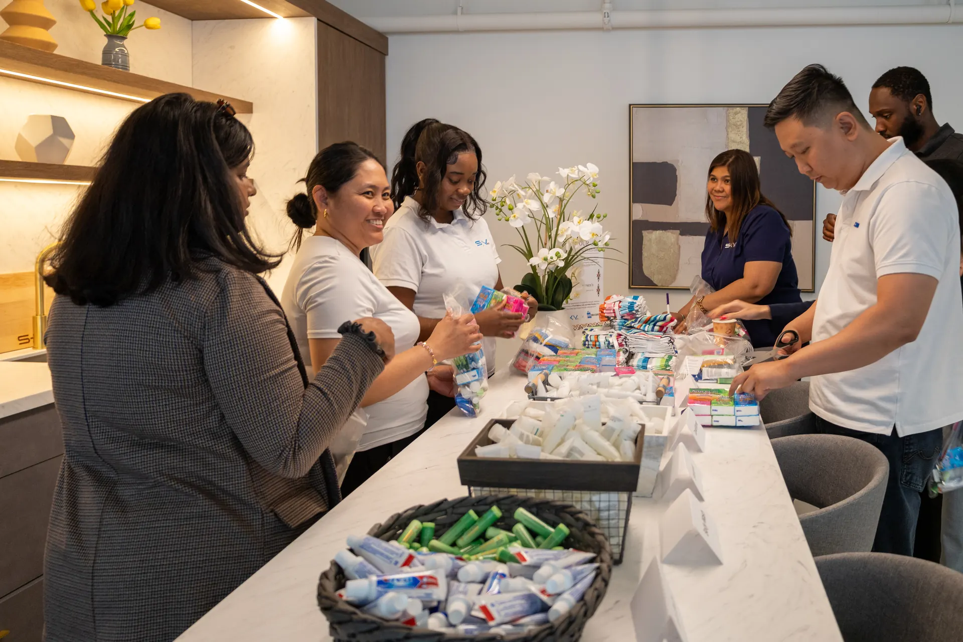Team members sorting toothpaste, soap and toiletries into care kits along the office kitchen counter