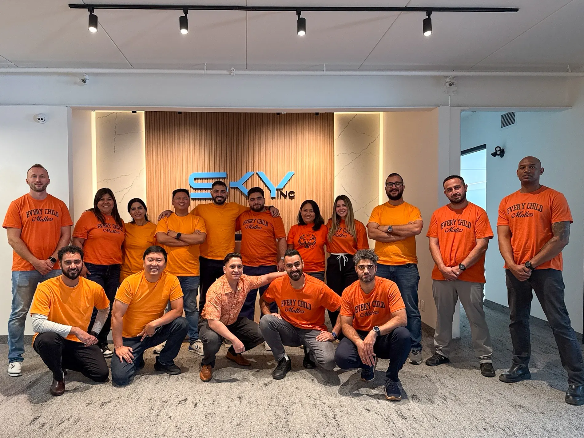 Sky Group team in orange Every Child Matters shirts in front of the SKY Inc reception wall