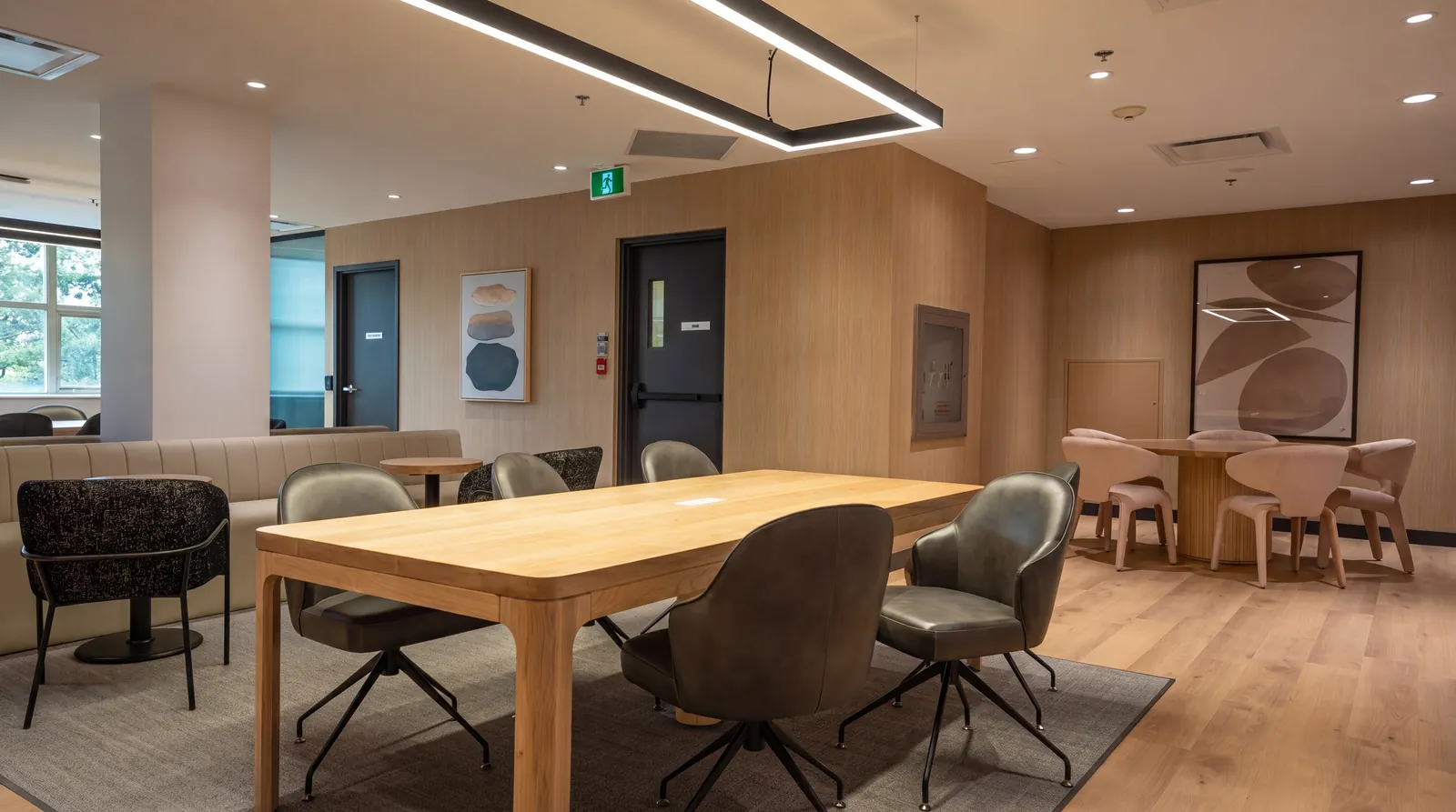 Coworking space with a white-oak work table, upholstered task chairs, banquette seating and wood wall panelling