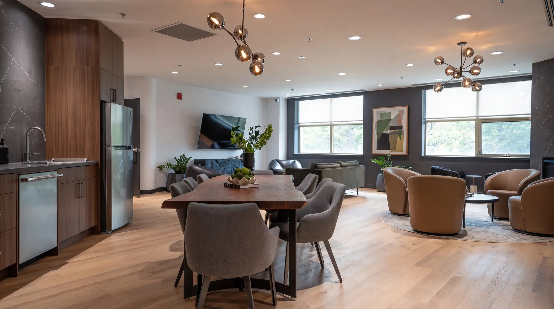 Social lounge with walnut kitchen millwork, stainless appliances, a long wood dining table and swivel lounge chairs