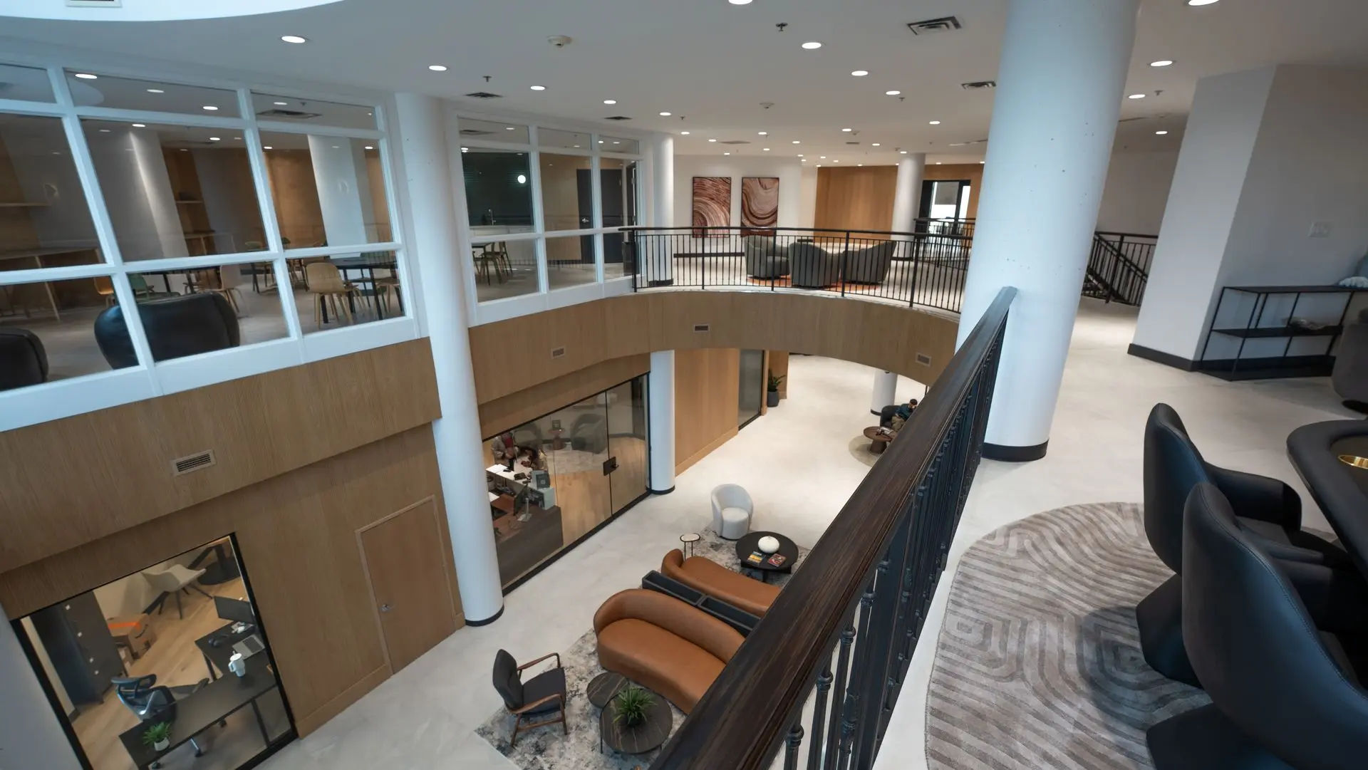 View down into the two-storey atrium: the lobby lounge below, glass-walled offices and the curved mezzanine railing