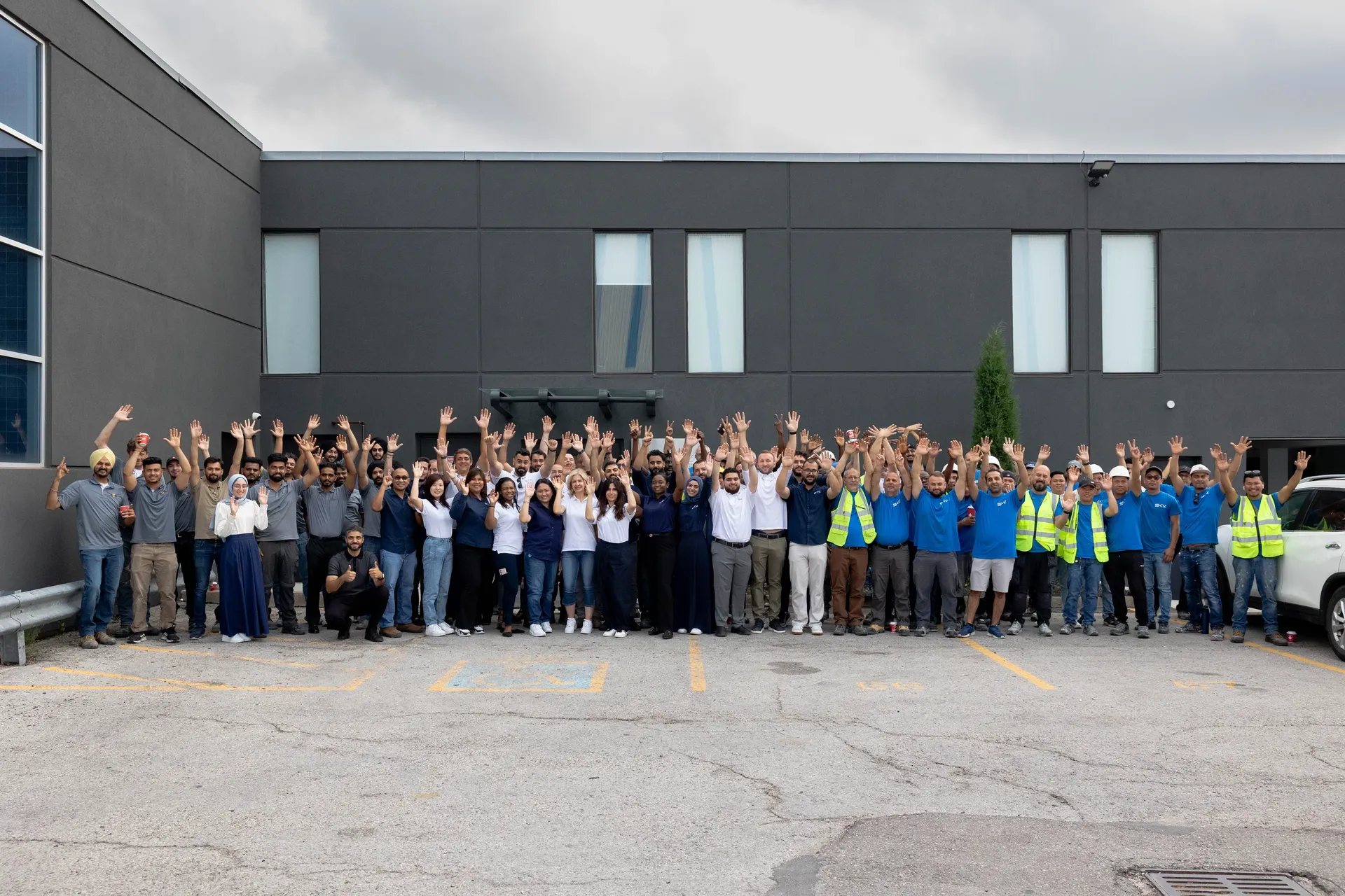 The Sky Group team — over a hundred people, arms raised, in front of the Oakville head office